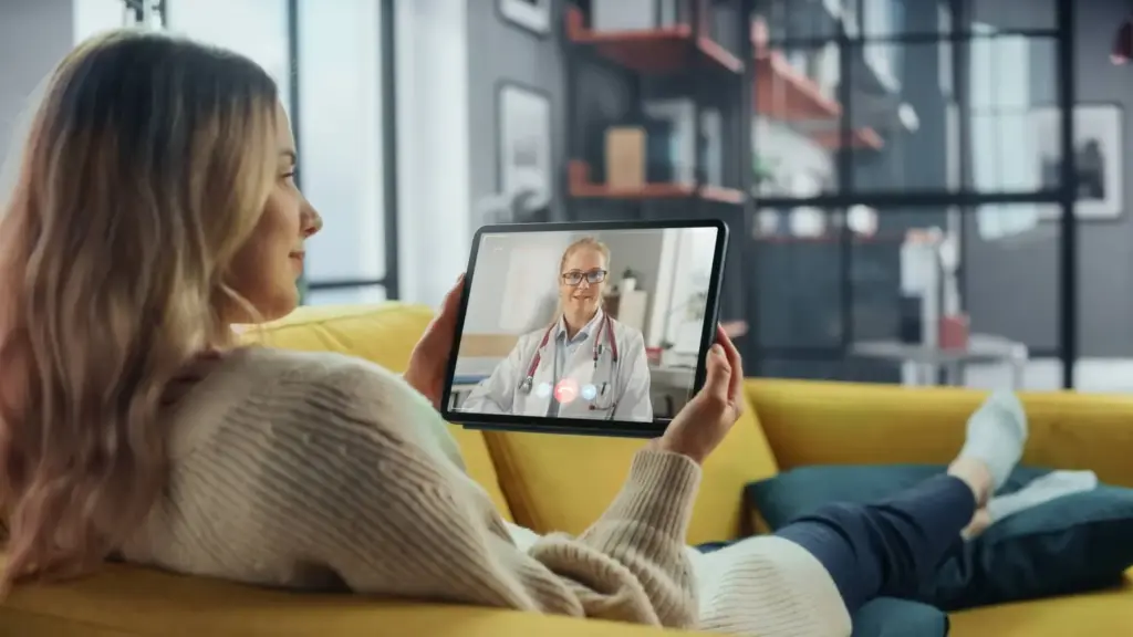 A woman relaxing on her sofa during a video visit with her practitioner on a tablet
